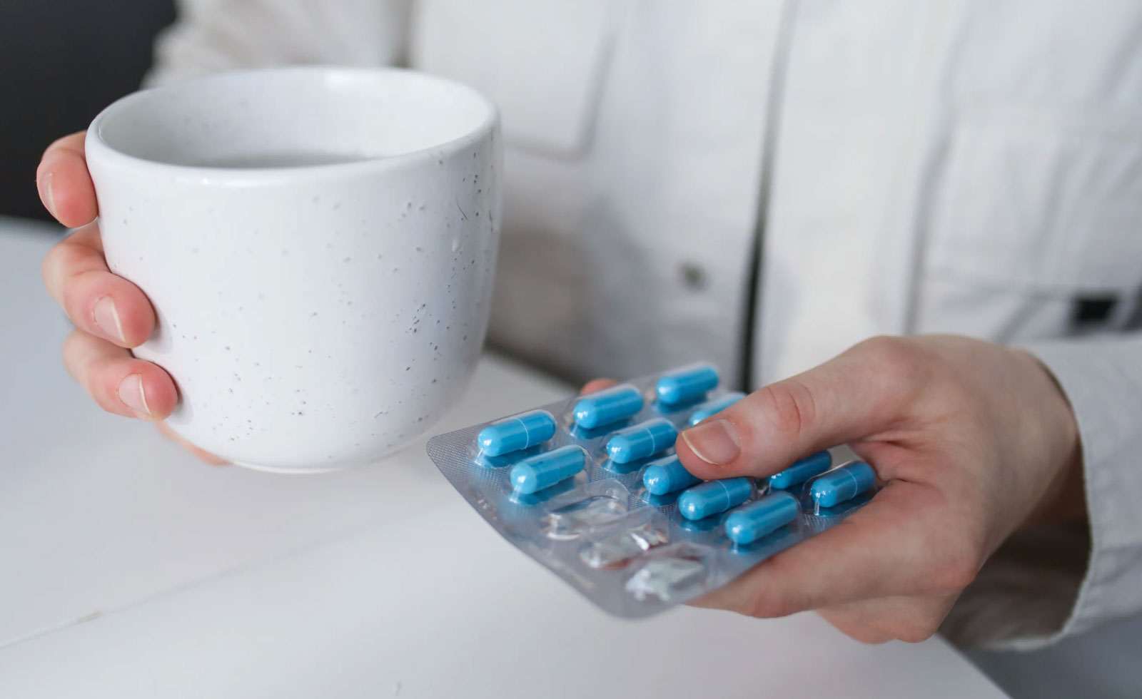 a person holding a packet of blue medication pills and a large cup