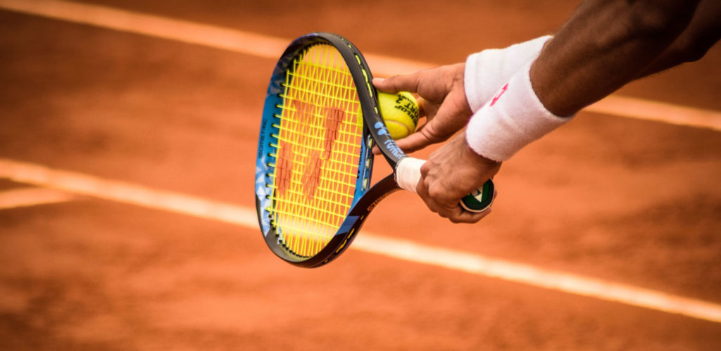 a close up photo of a person holding a tennis racquet and tennis balls on a clay court