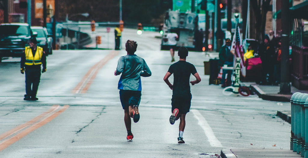 two marathon runners neck and neck running through a city street