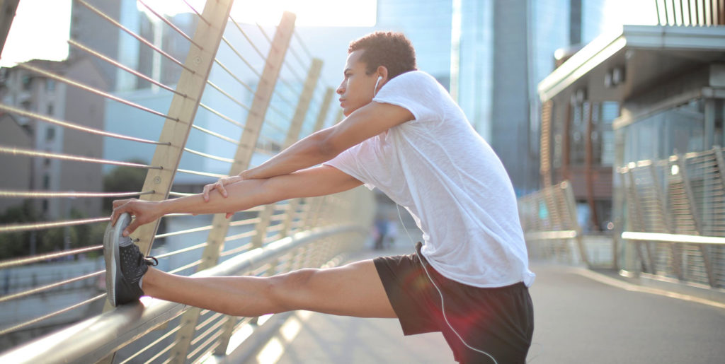 a man doing leg stretches on a fence in a city