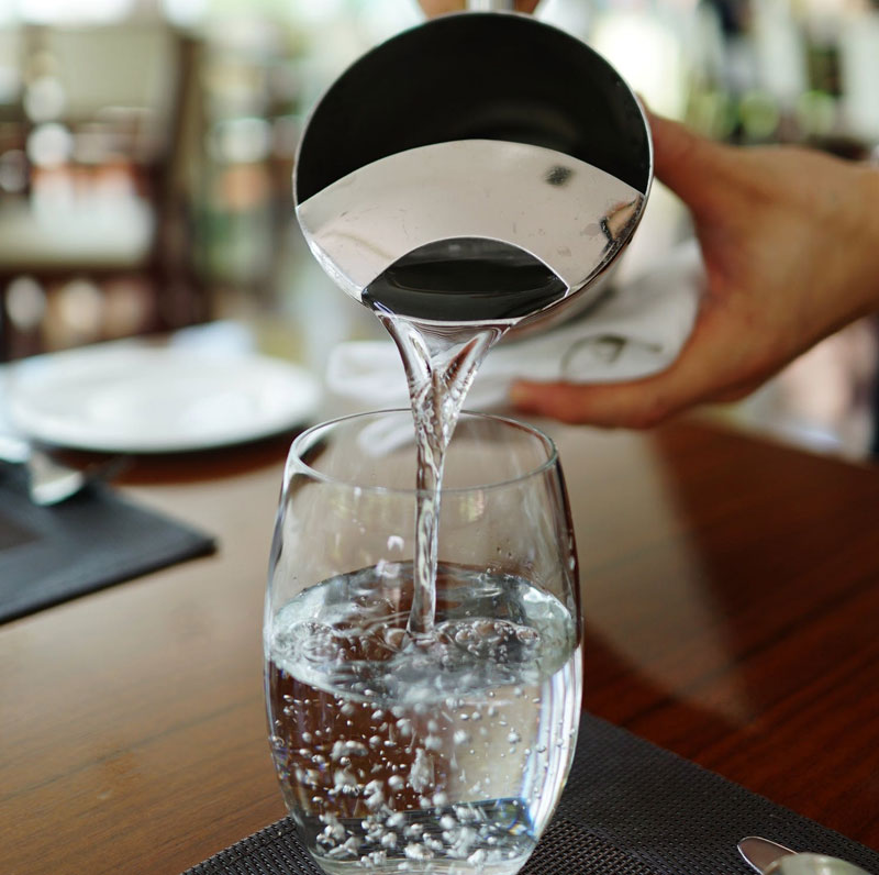 a person pouring water from a metal jug into a glass