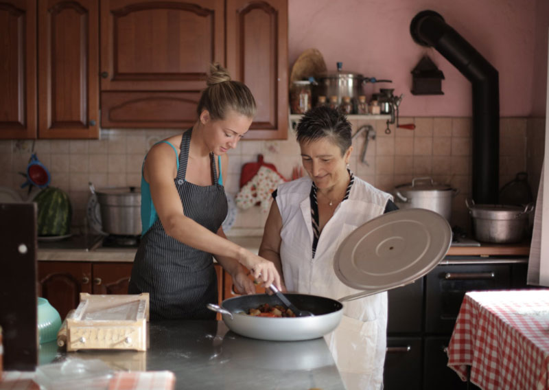 a mother and her adult daughter cooking a roast together in the kitchen