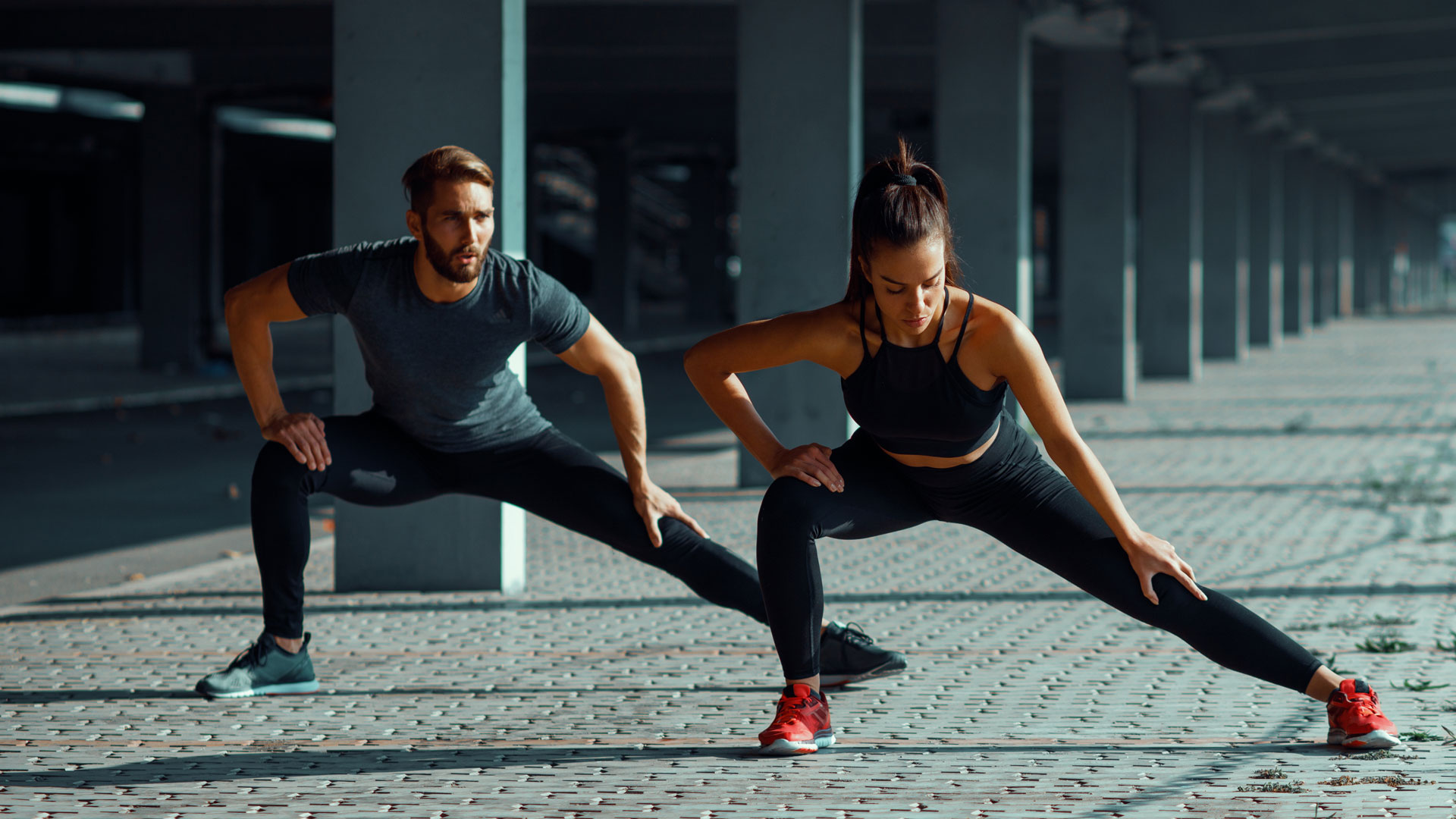 a man and woman in sportswear and sneakers stretching outdoors