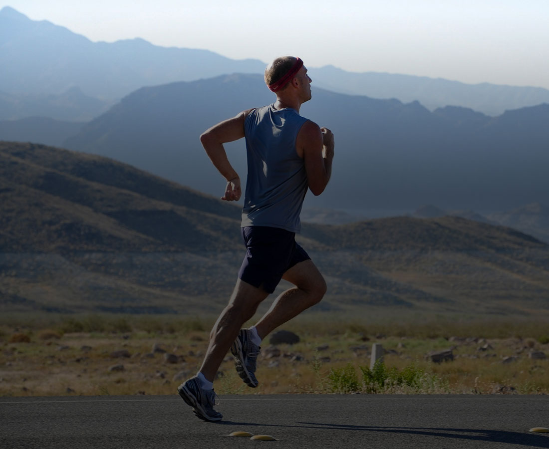 a man in a light blue top and headband running on a road near mountains