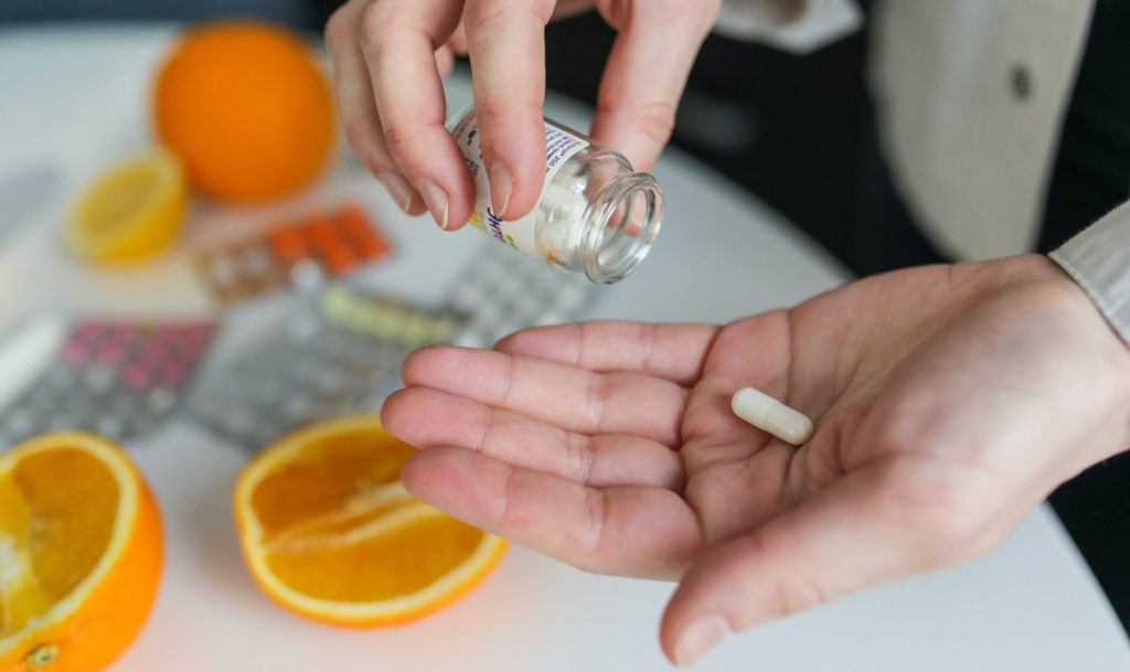 a close up photo of a person pouring a pill from a jar into their hand with oranges in the background