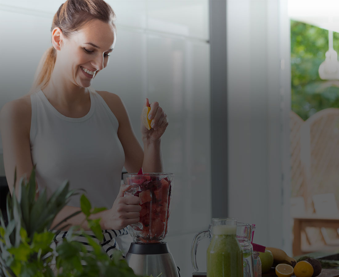 a woman smiling and blending a fruit smoothie