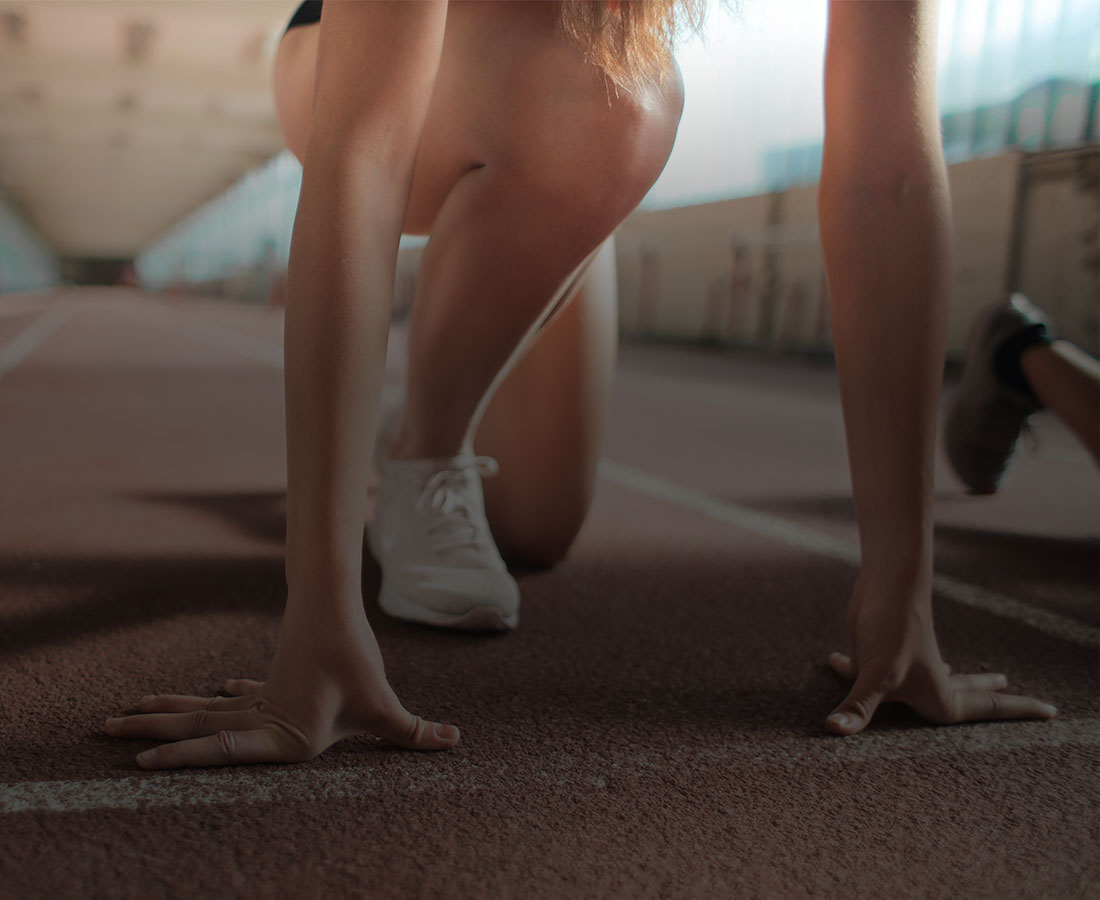 a woman in white sneakers in start position on an indoor athletics track