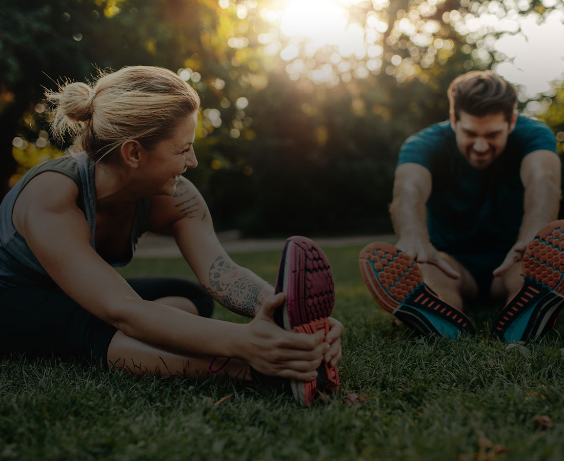 a man and woman in activewear stretching in the park together