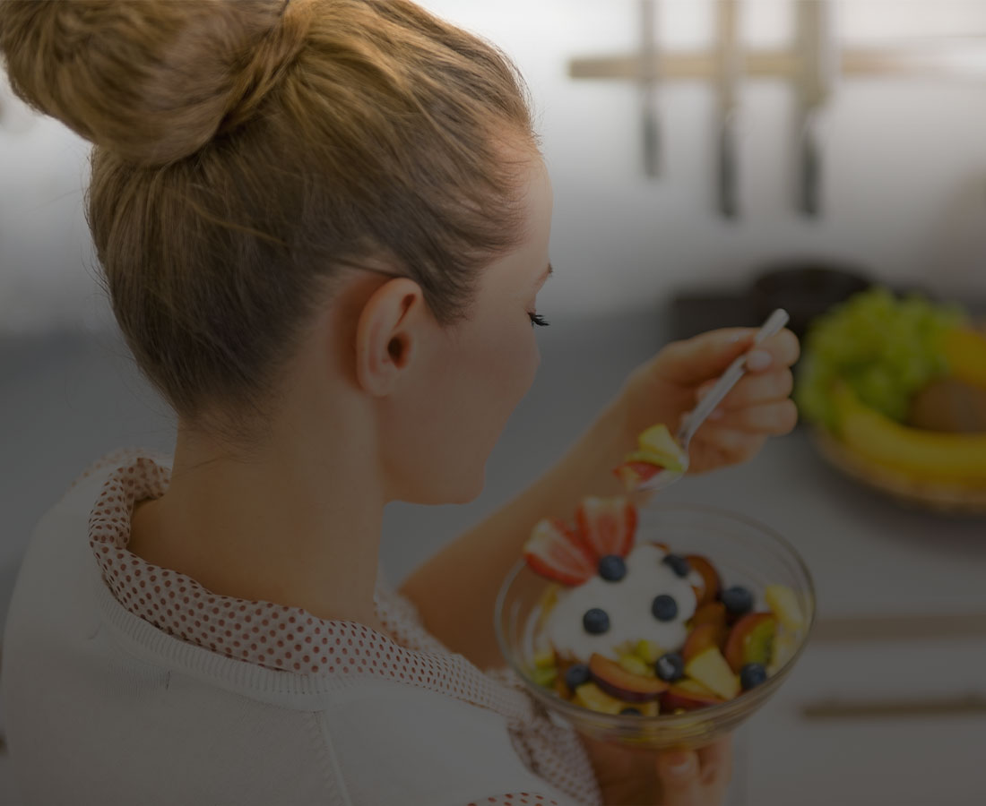 an over the shoulder shot of a woman eating a fruit salad dish
