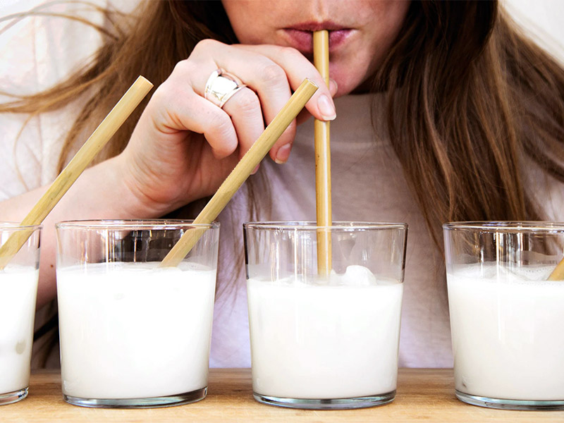 a woman drinking milk out of a glass using a bamboo straw