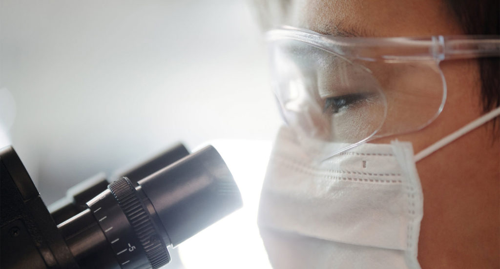 Close up of a scientist in a laboratory looking down a microscope