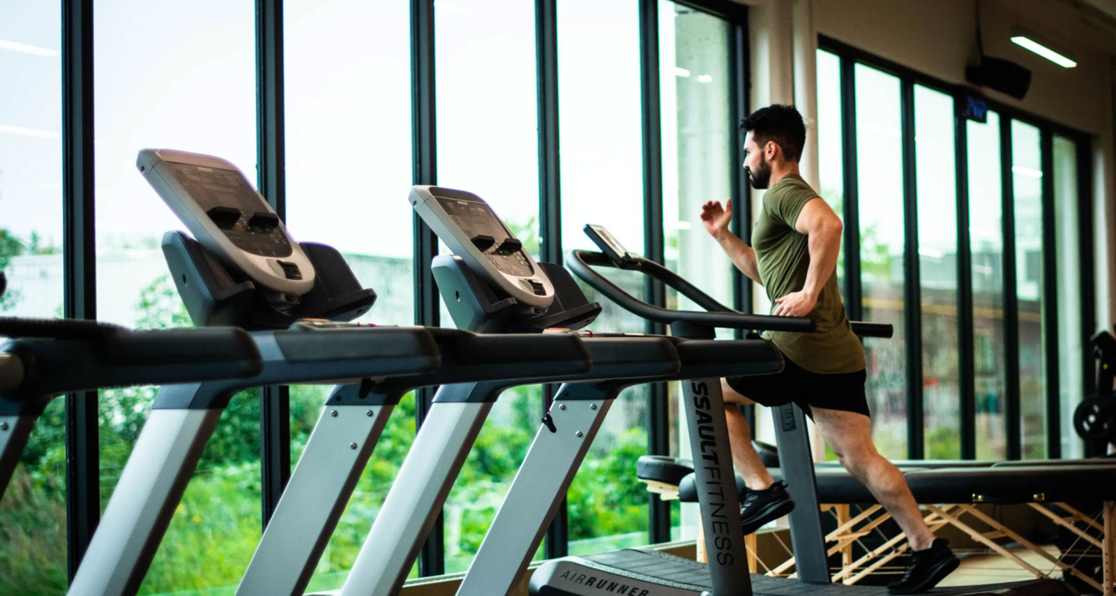 a man in a green top running on a treadmill in a gym