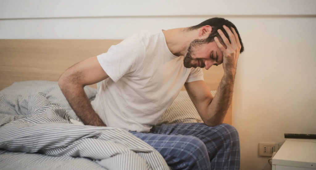 a man sitting up in bed suffering from pain