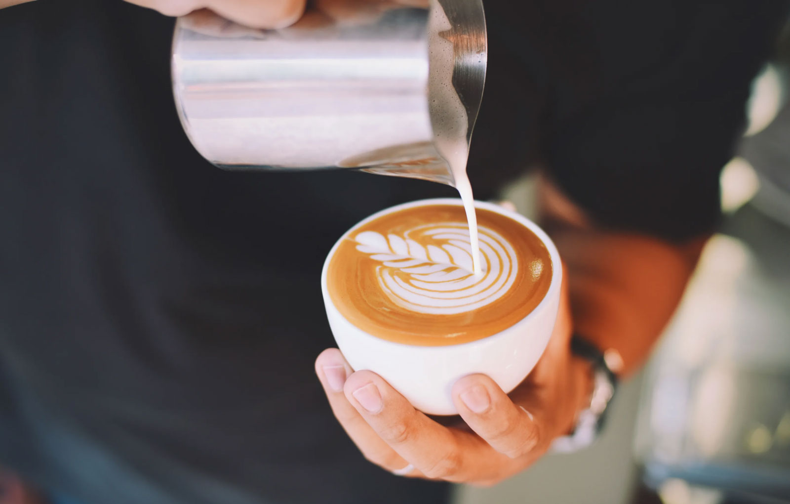 a barista pouring milk into a coffee cup to create a pattern on top