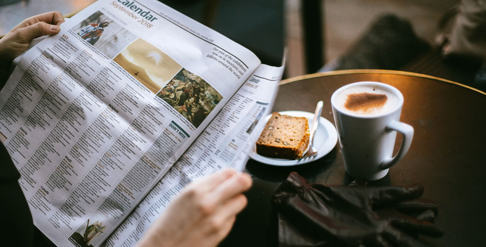 a person sitting at a table reading a newspaper with a cup of coffee and slice of toast