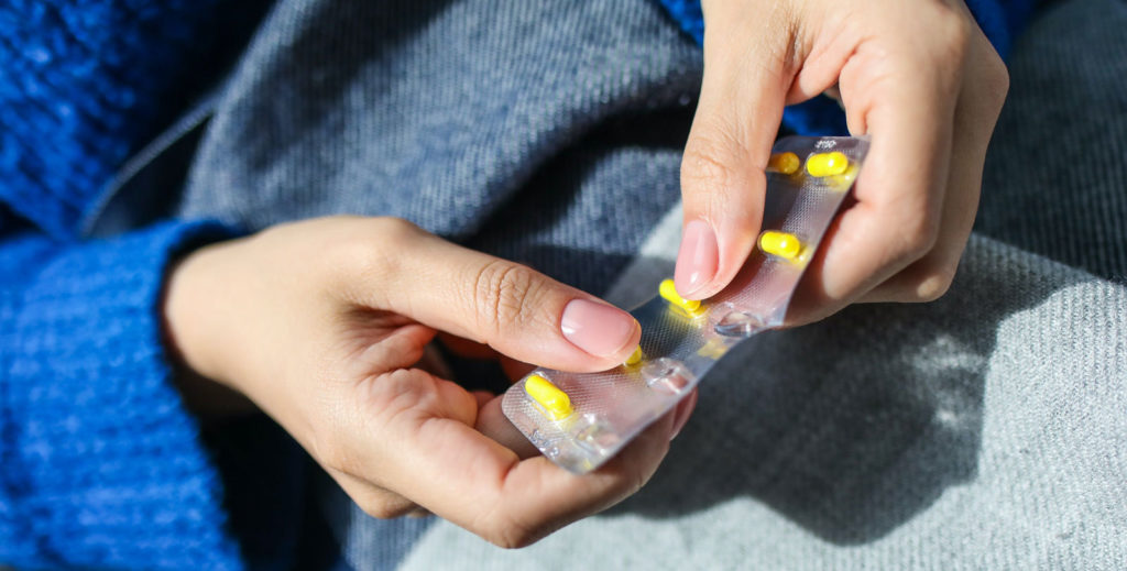 a person in a blue sweater taking pills out of aluminium packaging