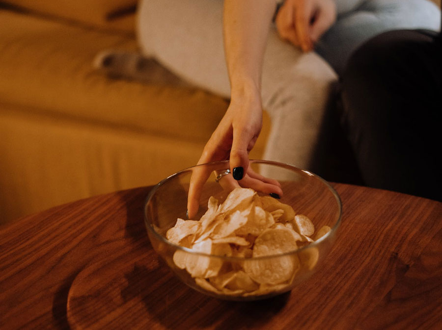 bowl-of-chips-on-table a person reaching for a bowl of potato chips on a table