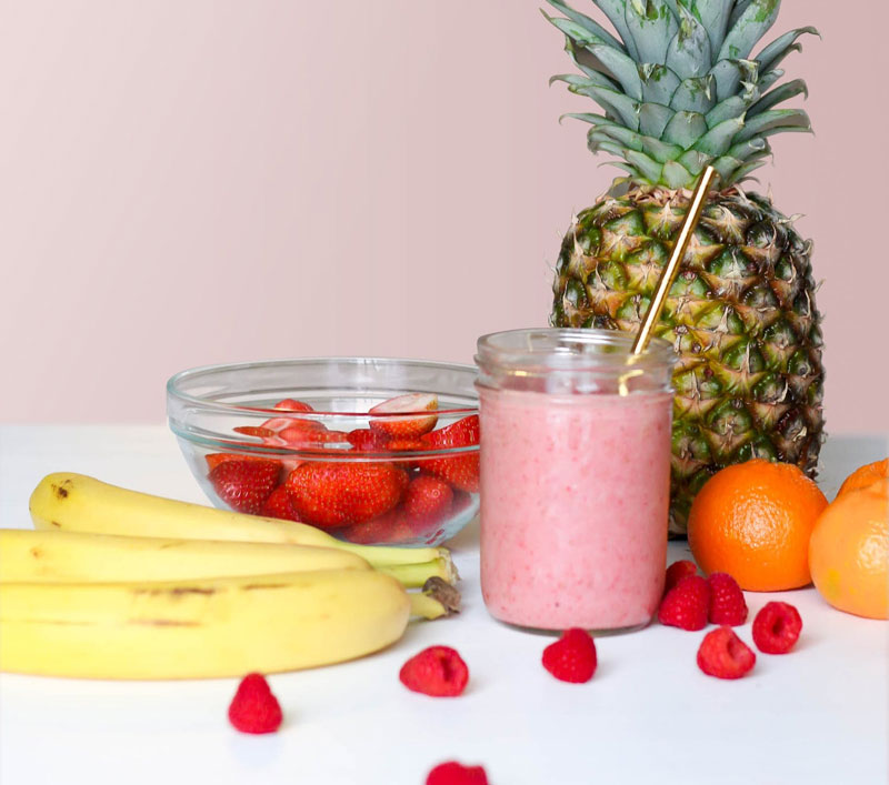 a fruit smoothie surrounded by various fruits on a table