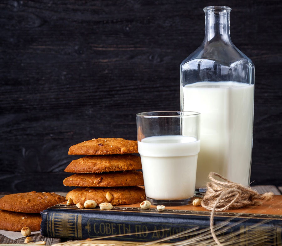 milk-and-cookies-on-table a bottle and glass of milk on a table with anzac cookies