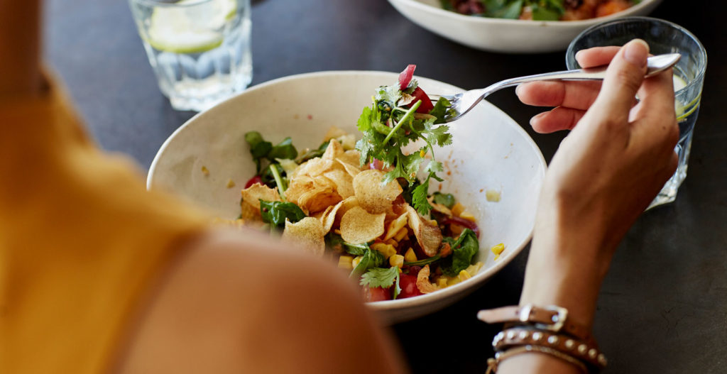 a woman photographed over the shoulder eating a delicious salad