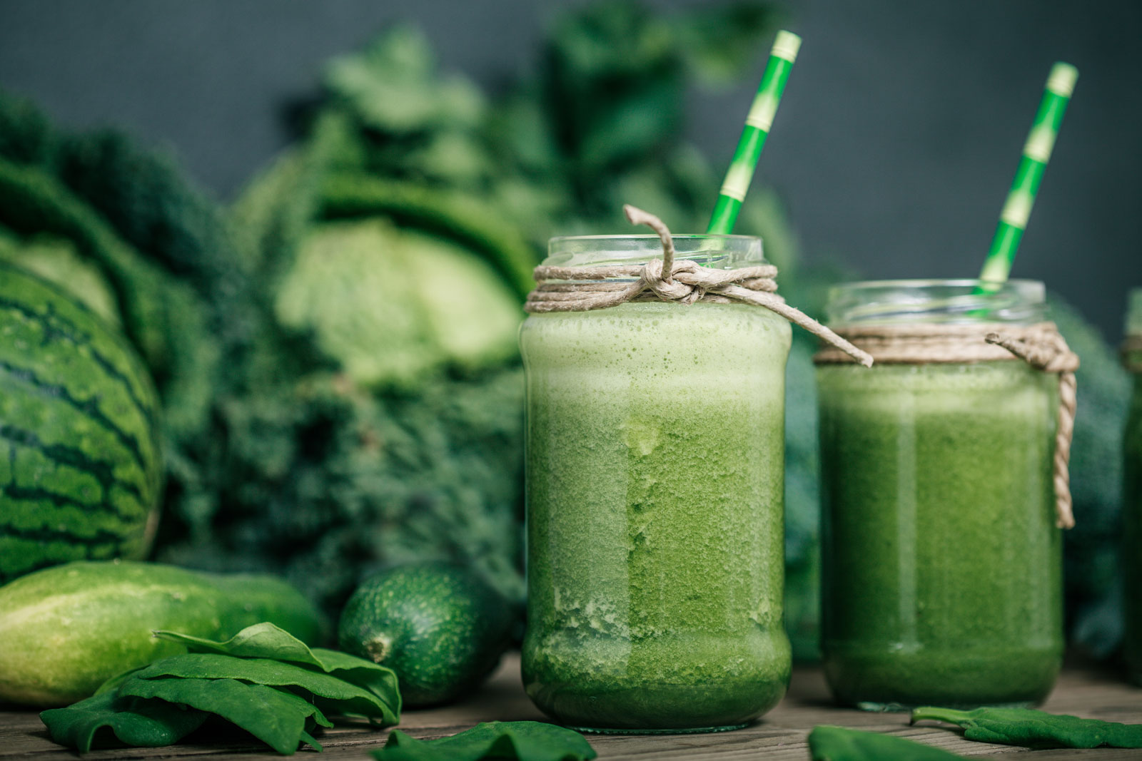 a photo of 2 green smoothies in glass jars on a table surrounded with greenery