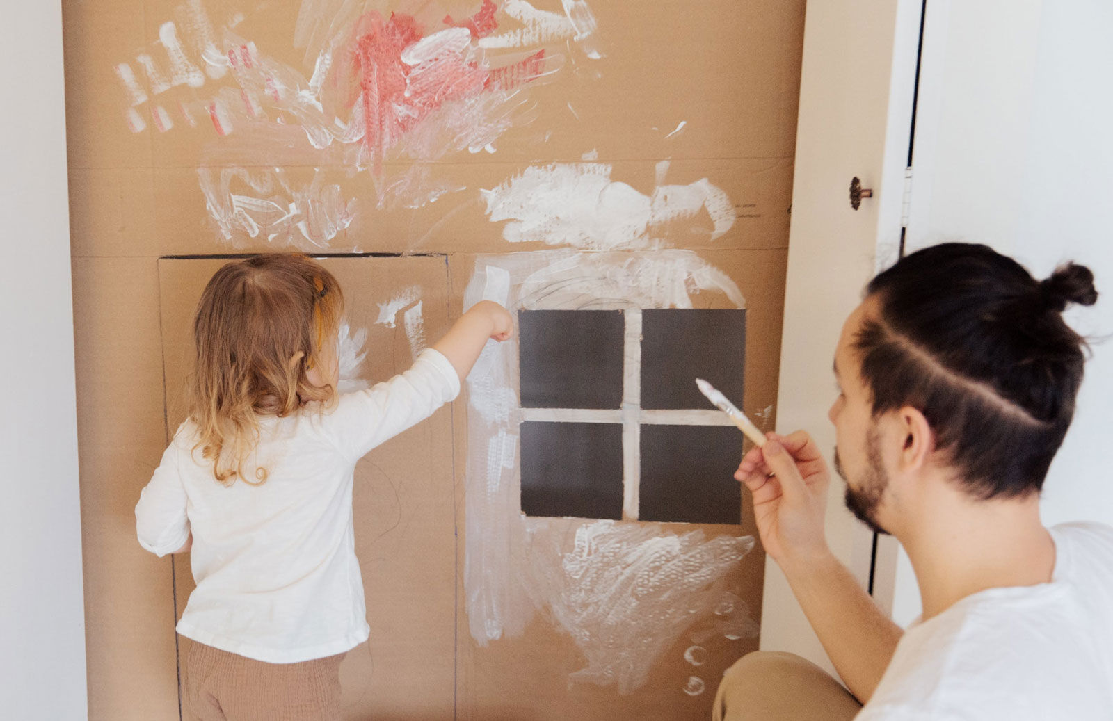 a father and his young daughter painting a carboard playhouse