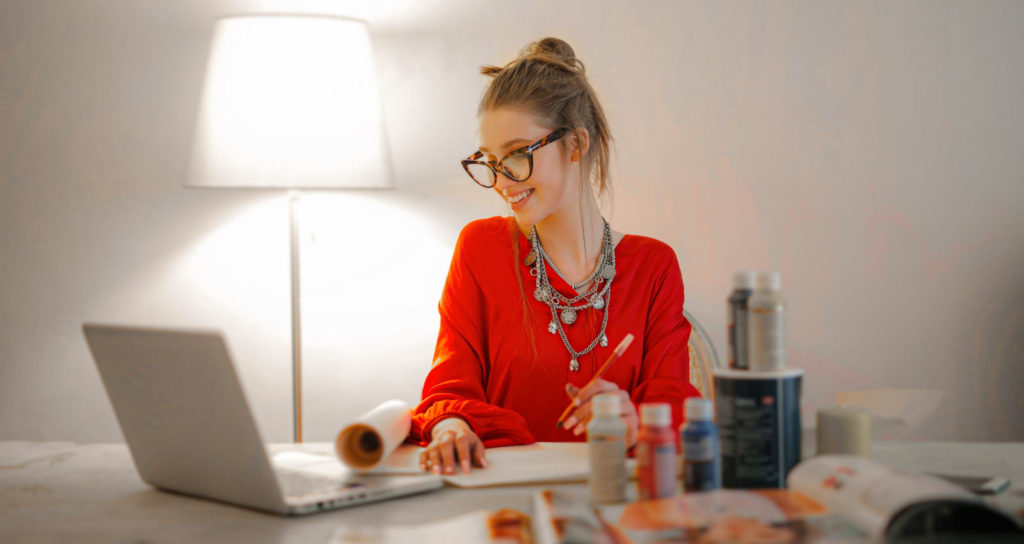 A woman in a red shirt working at home indoors on a laptop