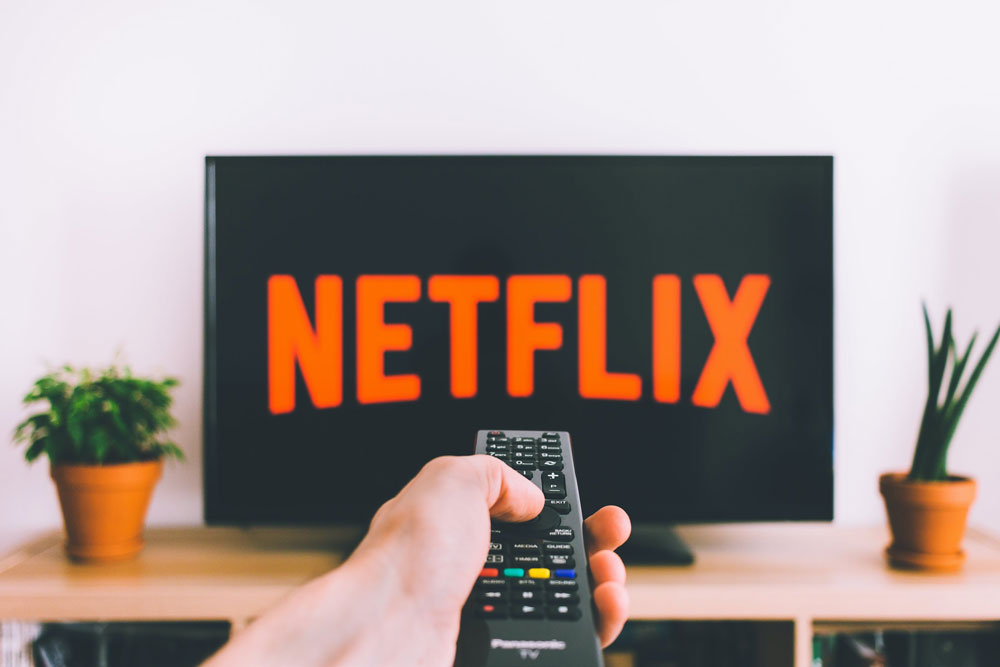 netflix-screen-time a person pointing the TV remote at a screen with Netflix
