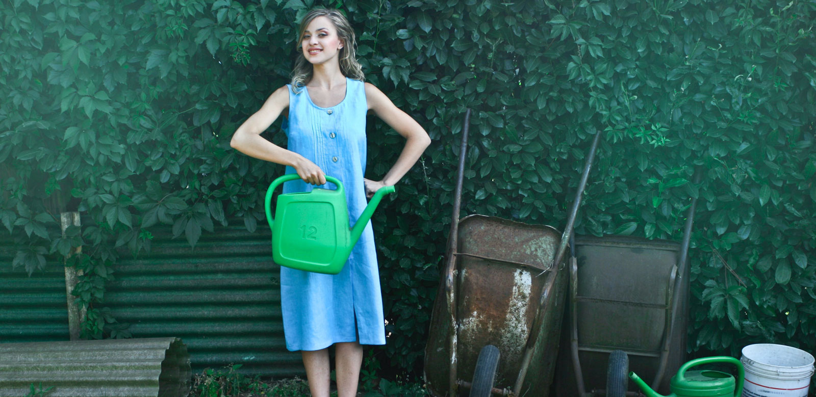 a woman in a blue dress posing with a watering can in her garden