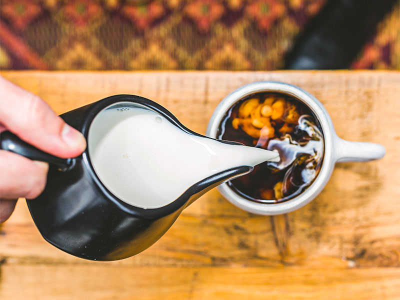 person pouring milk from a jug into a cup of coffee