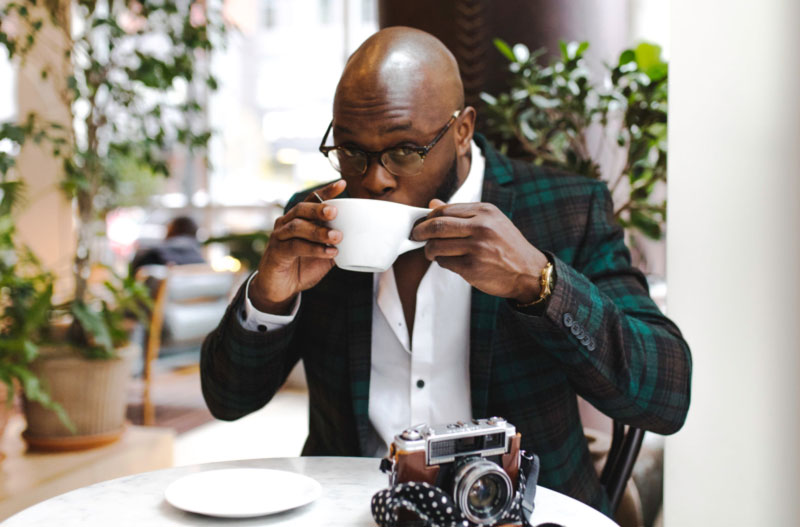 a man drinking coffee from a mug at a table with a vintage camera