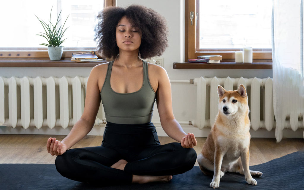 a woman at home in lockdown meditating on a yoga mat with a dog