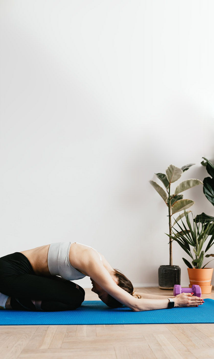 a woman in sports clothes doing yoga at home on a blue yoga mat with plants in the background