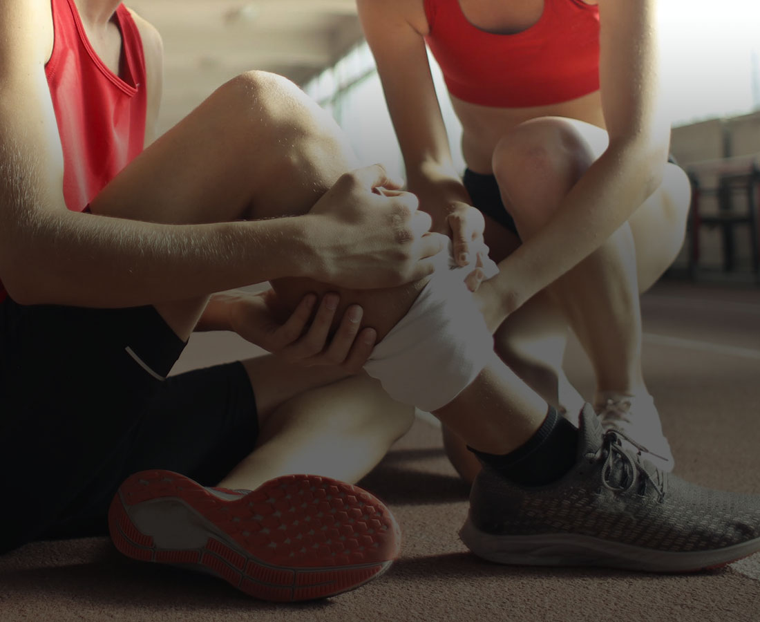 a man sitting on an athletics track while a second person is applying a bandage to his leg
