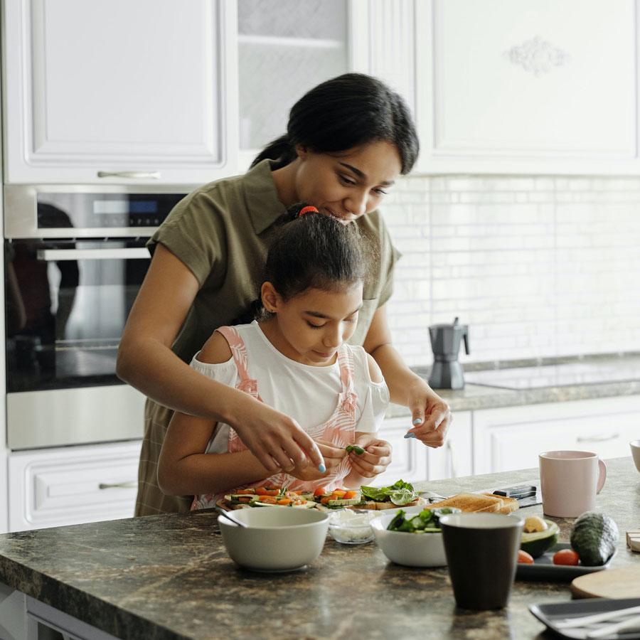 a mother and her young daughter together in the kitchen preparing avocado on toast