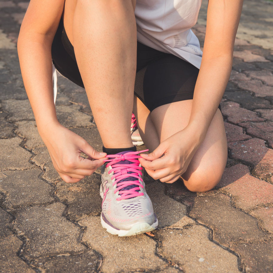 a close up shot of a person wearing running gear bending down to tie shoes