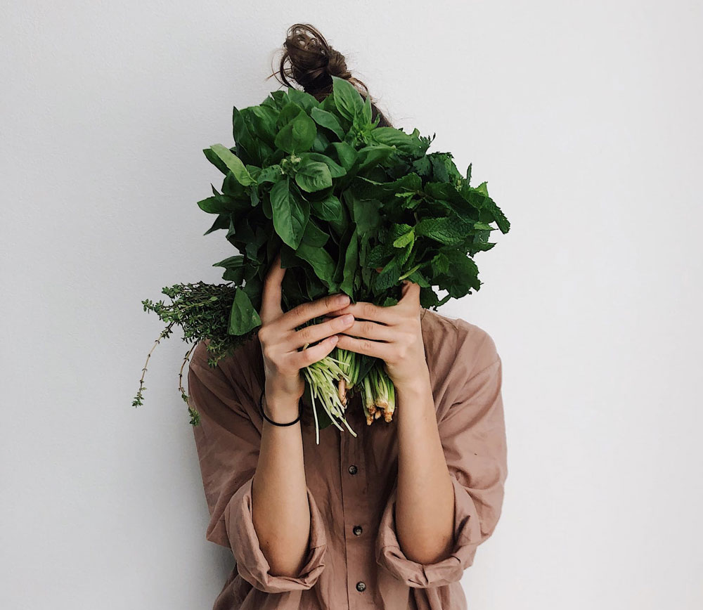 a woman in an earthy shirt holding leafy green vegetables in front of her face