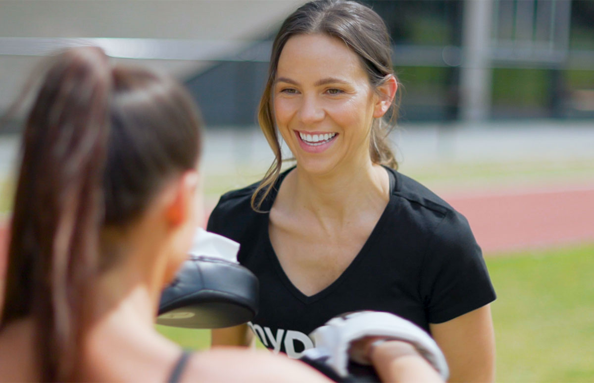 a selective focus photo of Alex Pendlebury smiling and practicing boxing outside at Olympic Park