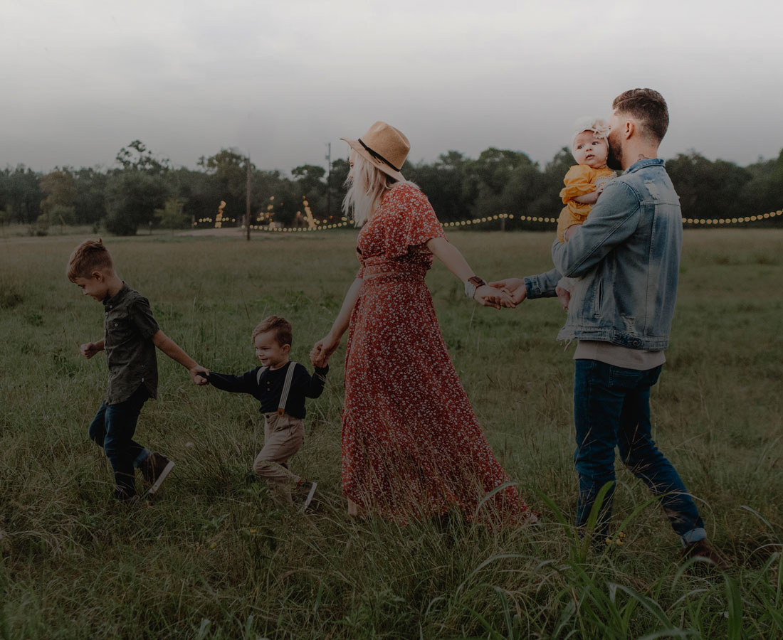 a family with 3 young kids walking through a grassy field holding hands