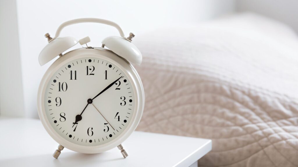A white analog clock sitting on a bedside table.