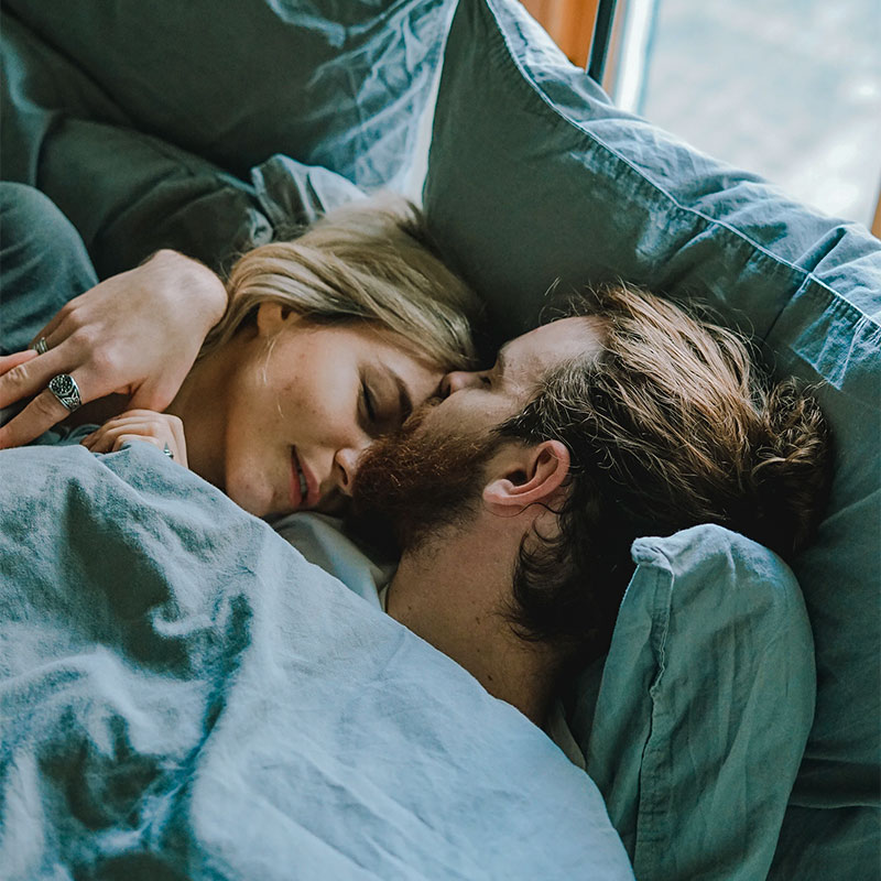 a husband and wife lying asleep in a blue bed together