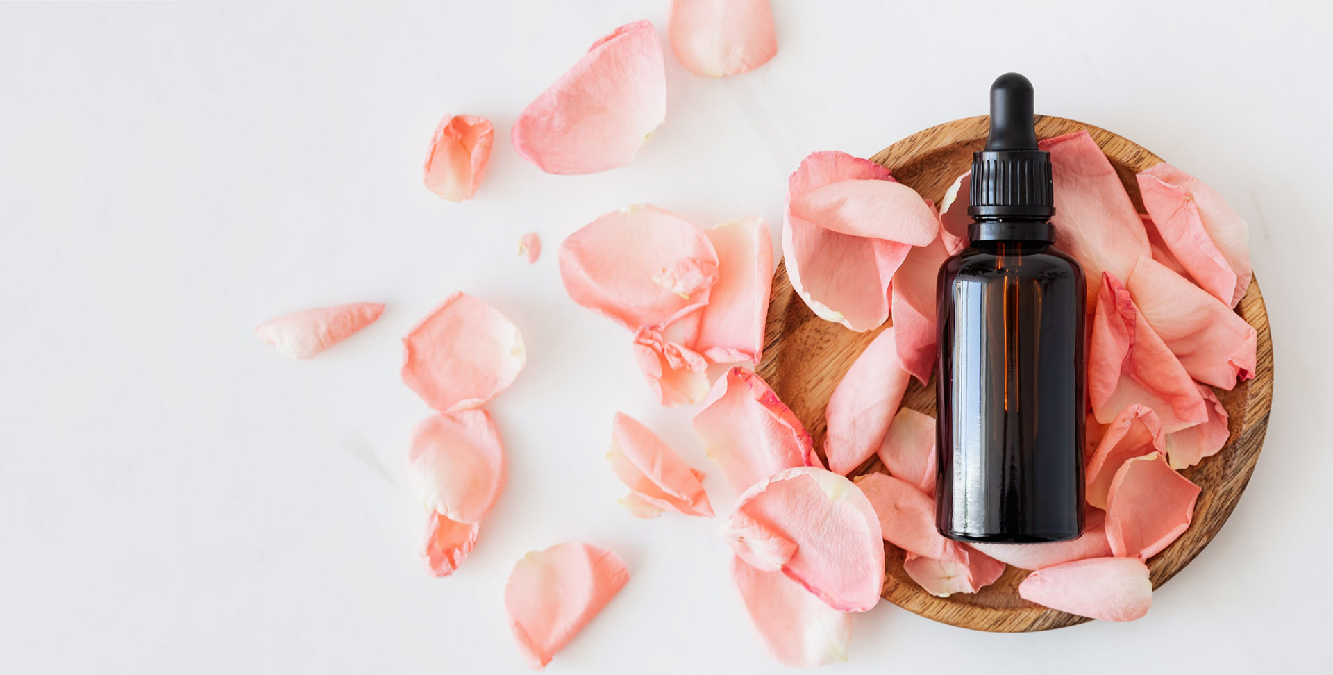 a small container of personalised skin care product with rose petals on a white background