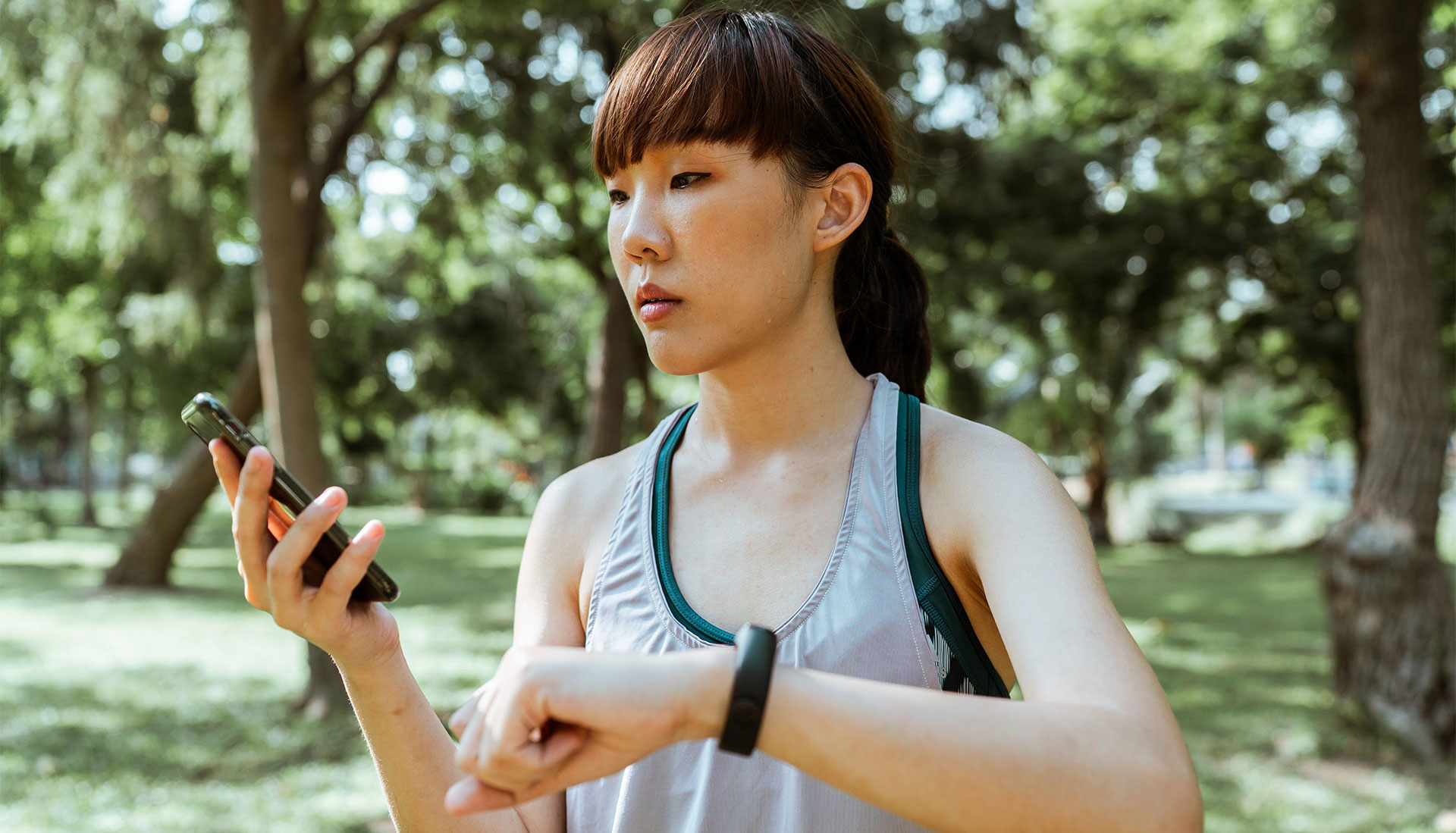 a woman in a grey sports top using her phone to compare fitness apps outdoors